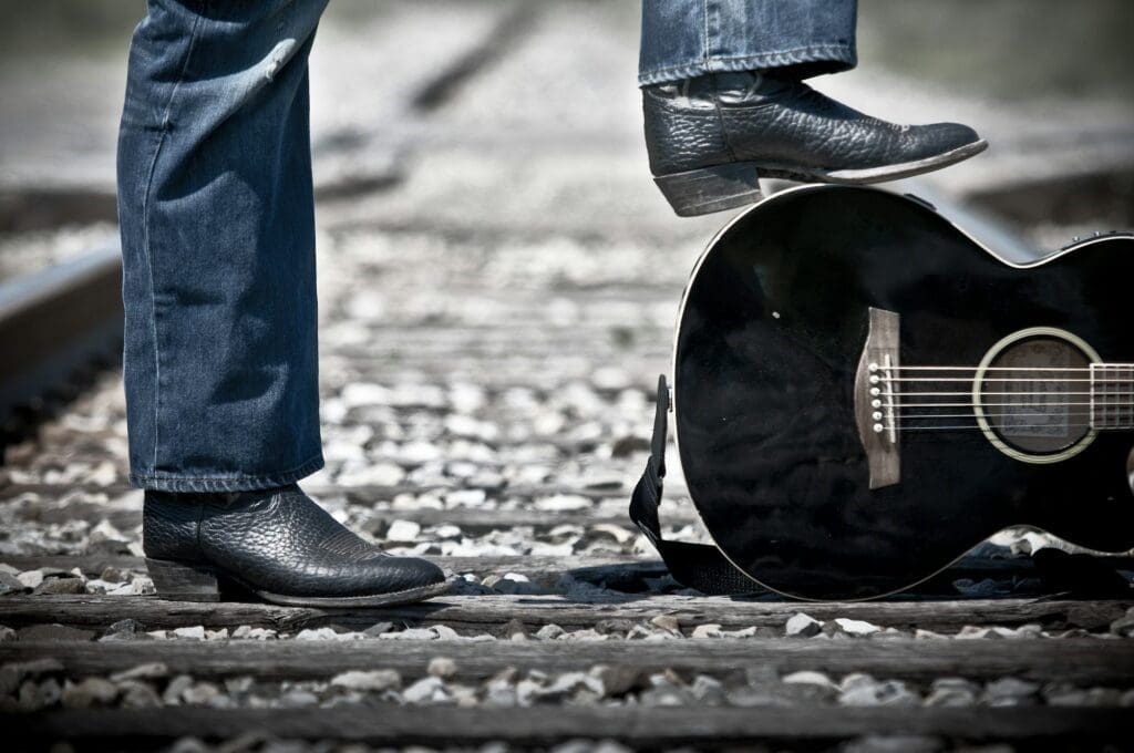 Male standing on train tracks with one foot on a guitar